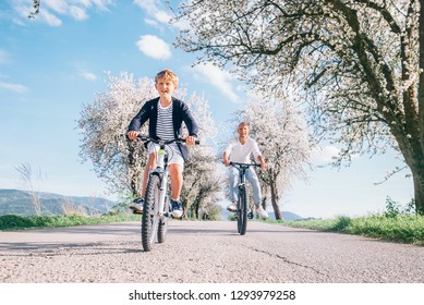 Father and son having fun when riding bicycles on country road under blossom trees. Healthy sporty lifestyle concept image. - Shutterstock ID 1293979258