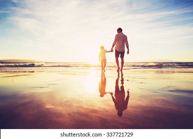 Vater und Sohn, die bei Sunset zusammen am Strand spazieren gehen