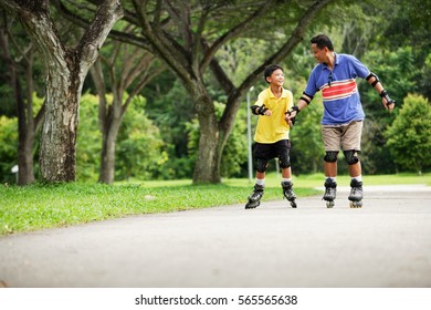 Father and son in-line skating in park, father holding son's hand