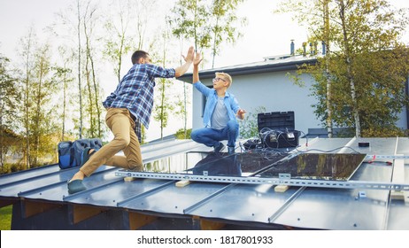 Father And Son Installing Solar Panels To A Metal Basis With A Drill. They Work On A House Roof And Give High Five. Concept Of Ecological Renewable Energy At Home And Quality Family Time.