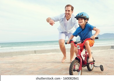 Father and son learning to ride a bicycle at the beach having fun together