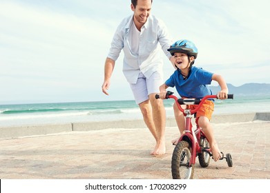 Father and son learning to ride a bicycle at the beach having fun together - Powered by Shutterstock