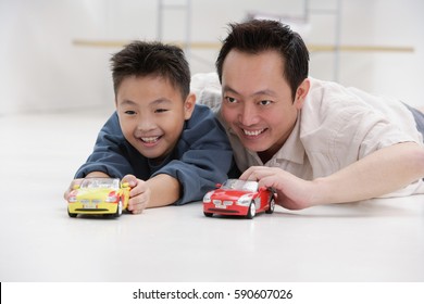 Father And Son Lying On Floor, Playing With Toy Cars