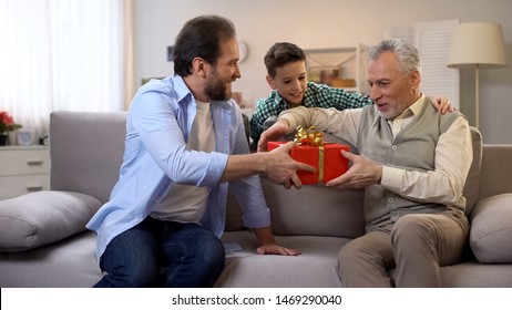 Father And Son Making Birthday Surprise For Senior Grandpa, Giving Gift Box