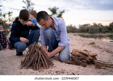 father and son making a campfire in the evening on the shore of the lake, dad teaching his teenage son how to make a campfire. Copy space