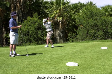 Father and son on the tee box. Son practicing, while father is looking at him.