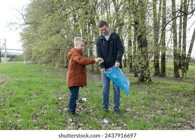 Father and son participating in a community clean-up, picking up litter in a park. Family volunteering and environmental care concept - Powered by Shutterstock