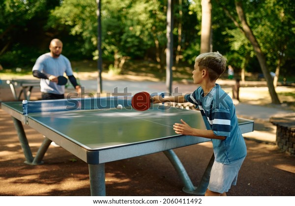 Father and son play\
table tennis outdoors