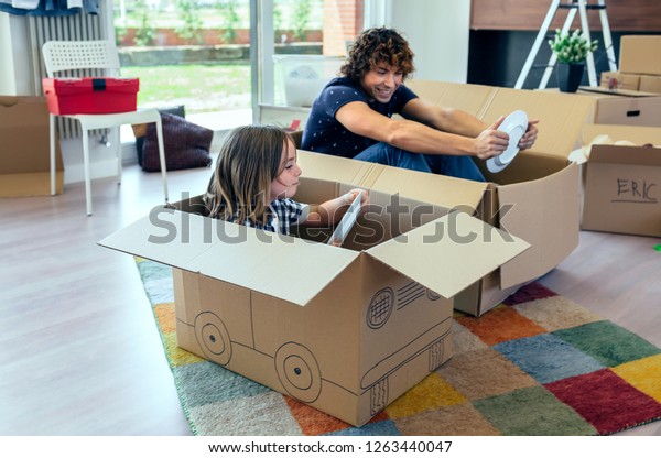 Father and son playing car racing with cardboard\
boxes in the living room