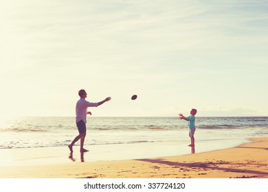 Father And Son Playing Catch Throwing Football On The Beach At Sunset