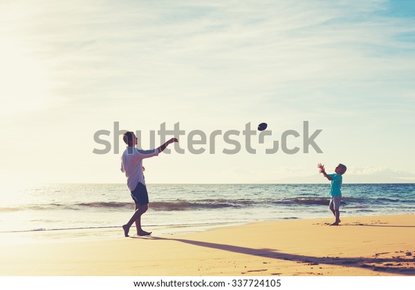 Father and Son Playing Catch Throwing Football on\
the Beach at Sunset