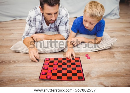 Father and son playing checker game while lying on hardwood floor at home