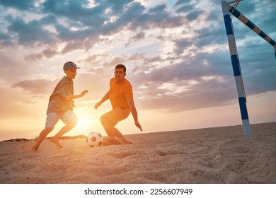 Father and Son playing football, family fun outdoors players in soccer in dynamic action have fun playing football in the beach, summer day under sunlight. - Shutterstock ID 2256607949