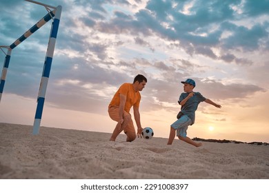 Father and Son playing football, family fun outdoors players in soccer in dynamic action have fun playing football in the beach, summer day under sunlight. - Shutterstock ID 2291008397