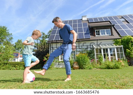 Father and son playing football in garden of solar paneled house