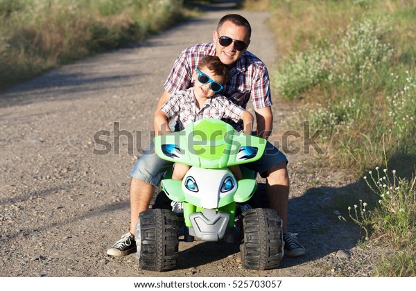 Father and son playing on the road at\
the day time. They driving on quad bike in the park. People having\
fun on the nature. Concept of friendly\
family.