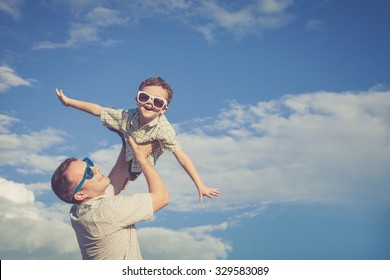 Father And Son Playing In The Park  At The Day Time. Concept Of Friendly Family. Picture Made On The Background Of Blue Sky.