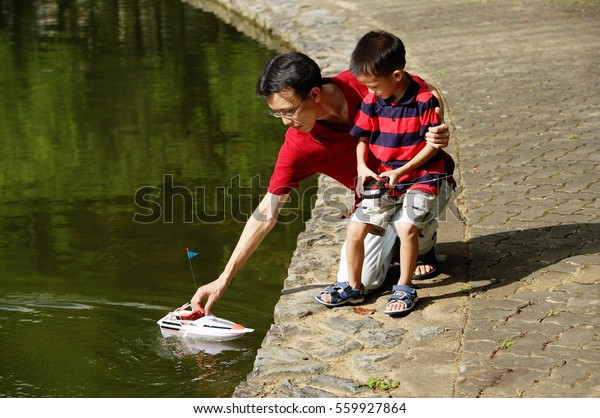 Father and son playing with remote control boat,\
father reaching for boat