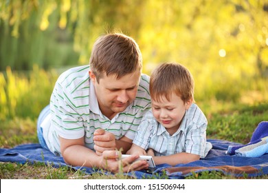 Father and son playing with smartphone  together outdoors