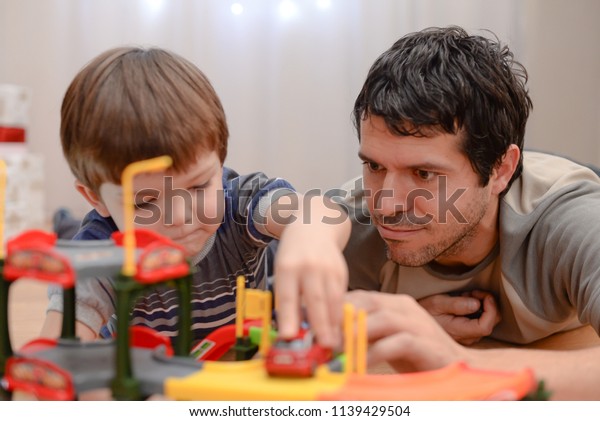 Father and son are playing with toy cars. Happy\
family playing with toys