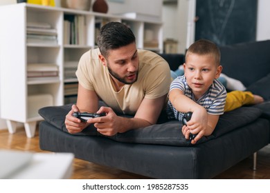 father and son playing video games with controllers at home - Shutterstock ID 1985287535