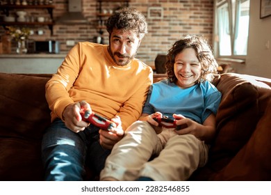 Father and son playing videos games on a gaming console in the living room of their home - Powered by Shutterstock