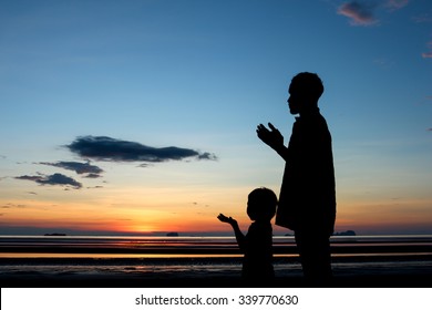 Father and son praying under sunset sky.