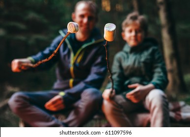 Father and son prepare to bake marshmallow candies on campfire