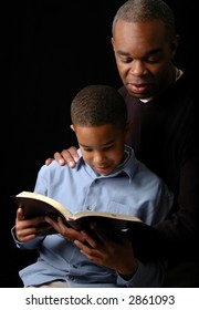 Father And Son Reading A Bible Over A Black Background.