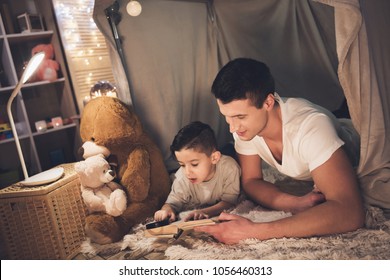 Father and son are reading book with magnifying glass in blanket fort at night at home. - Powered by Shutterstock