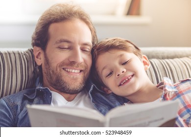 Father and son are reading a book and smiling while spending time together at home
