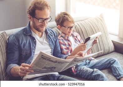 Vater und Sohn lesen Zeitungen und lächeln, während sie zu Hause Zeit zusammen verbringen