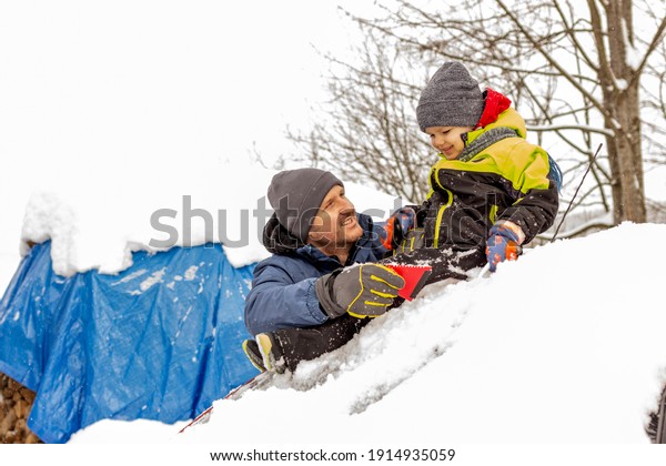 Father and son removing deep snow from car. Little\
boy helping his father to remove snow from family car after winter\
attack. Father and son are removing snow and ice from their car.\
Copy space.