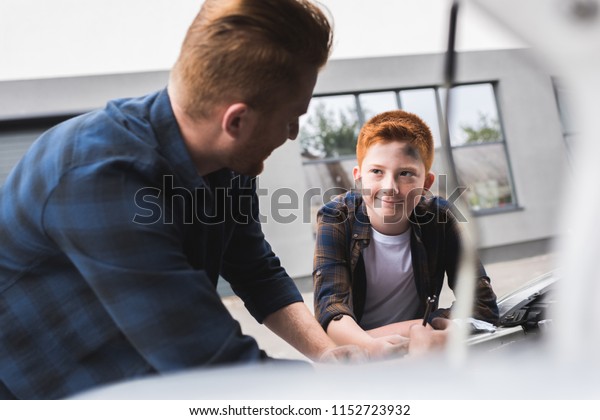 father and son repairing car with open hood and\
looking at each other