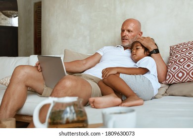 Father And Son Resting On Sofa. Portrait Of Dad With Little Boy Using Tablet And Enjoying Leisure On Summer Vacation At Tropical Villa. 