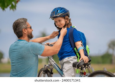 Father and son are riding bike together on summer weekend. Happy playful dad with excited kid son riding a bicycle on weekend. Father helping his son to wear a cycling helmet. Child in safety helmet. - Powered by Shutterstock