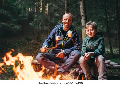 Father and son roast marshmallow candies on the campfire in forest. Spring or autumn camping  - Powered by Shutterstock