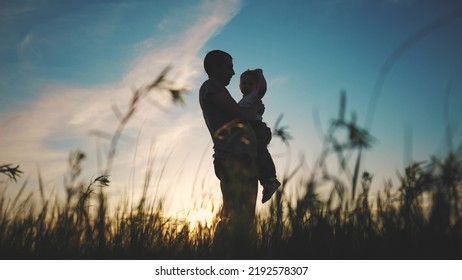 father and son silhouette. happy family kid dream concept. father holding in his arms in the grass in nature at sunset shadow silhouette. fathers day. father and son in sunset the park silhouette