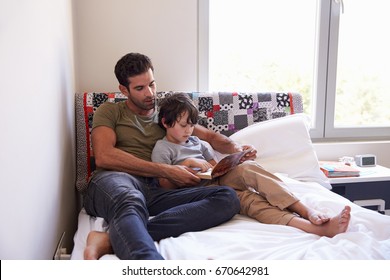 Father And Son Siting On Bed Reading Book Together