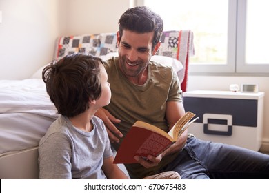 Father And Son Siting On Bedroom Floor Reading Book Together