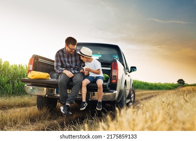 Father And Son Sits On Trunk Of Truck In Wheat Field