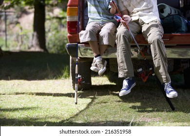 Father And Son Sitting With Fishing Poles On Edge Of Truck Bed