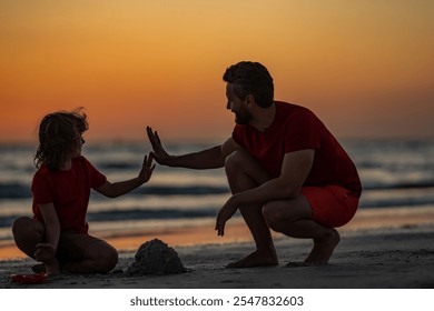 Father and son sitting on the beach of summer with sunset tone. Child and father building sandcastle. Father and son playing on summer beach. Father and child son playing with sand on sea. Sand castle - Powered by Shutterstock