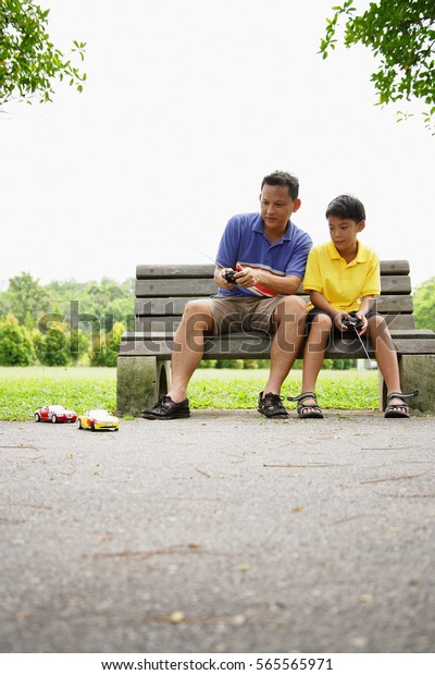 Father and son, sitting on bench, playing with\
remote control cars