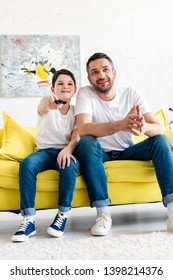 father and son sitting on couch and watching tv at home
