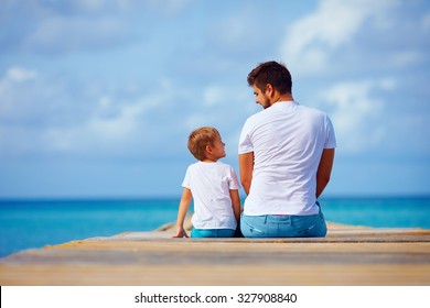Father And Son Sitting On Pier And Talk