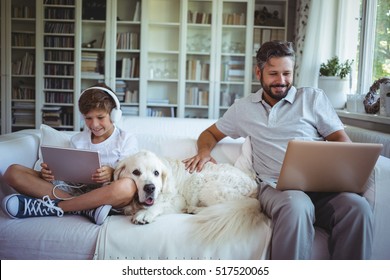 Father and son sitting on sofa and using digital tablet and laptop in living room at home