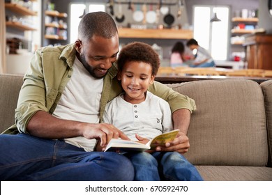 Father And Son Sitting On Sofa In Lounge Reading Book Together