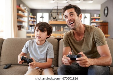 Father And Son Sitting On Sofa In Lounge Playing Video Game - Powered by Shutterstock