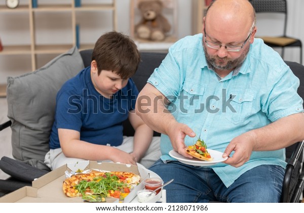 A father and son are sitting on the sofa sharing\
slices of pizza.